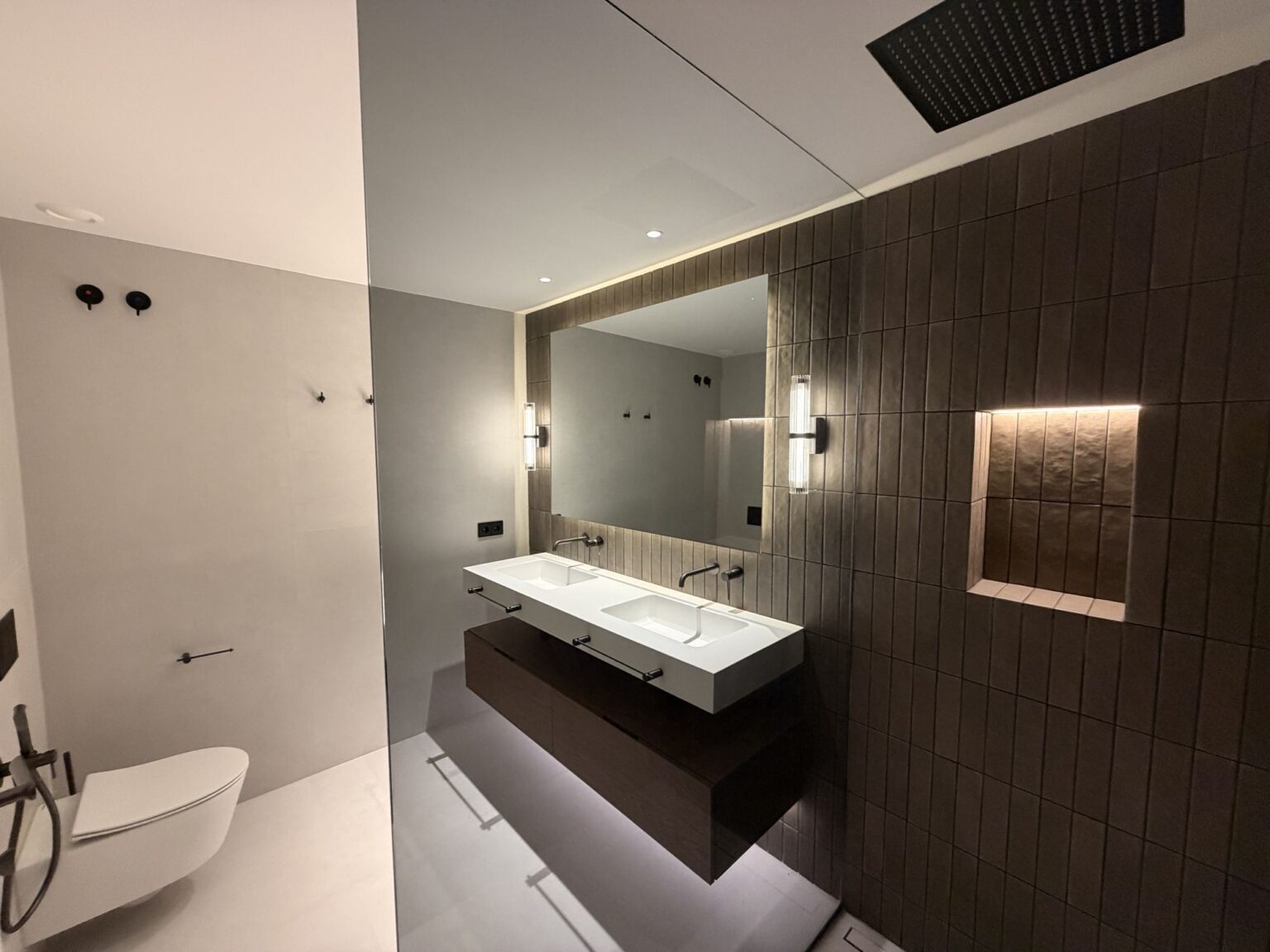 Baño con lavabo suspendido, espejo retroiluminado y revestimiento cerámico